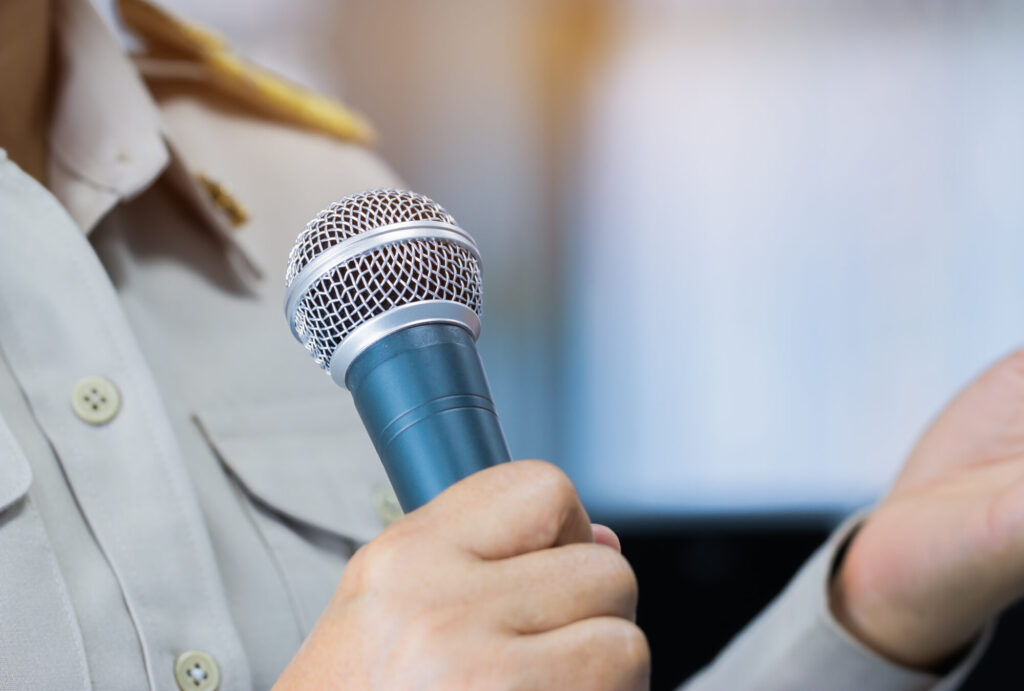 Thai Teacher Speaking in classroom or Conference meeting hall with Microphone of speech in seminar room on hall light bokeh background. Speaker Business tedtalk is vocalized form communication humans.